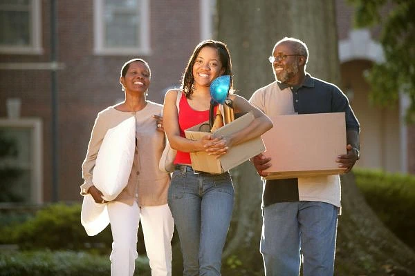 A cheerful family carries belongings while moving outdoors on a sunny day.